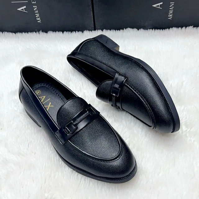 Black formal men's dress shoes displayed on a wooden table near books and window.