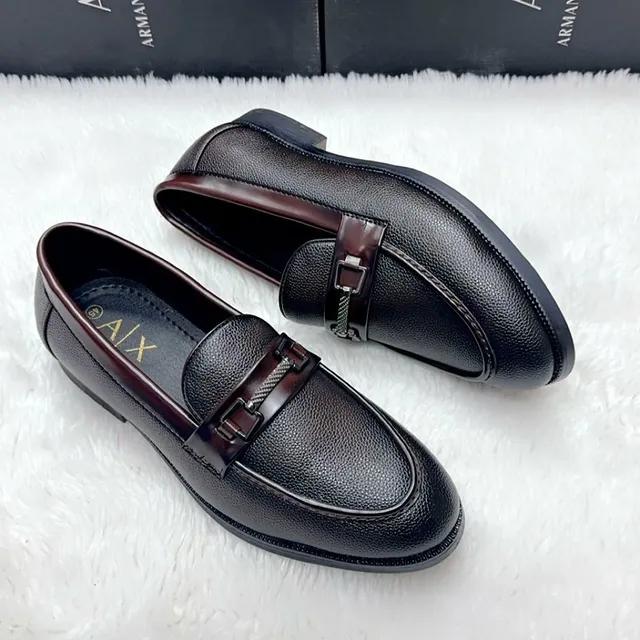 Black formal men's dress shoes displayed on a wooden table near books and window.