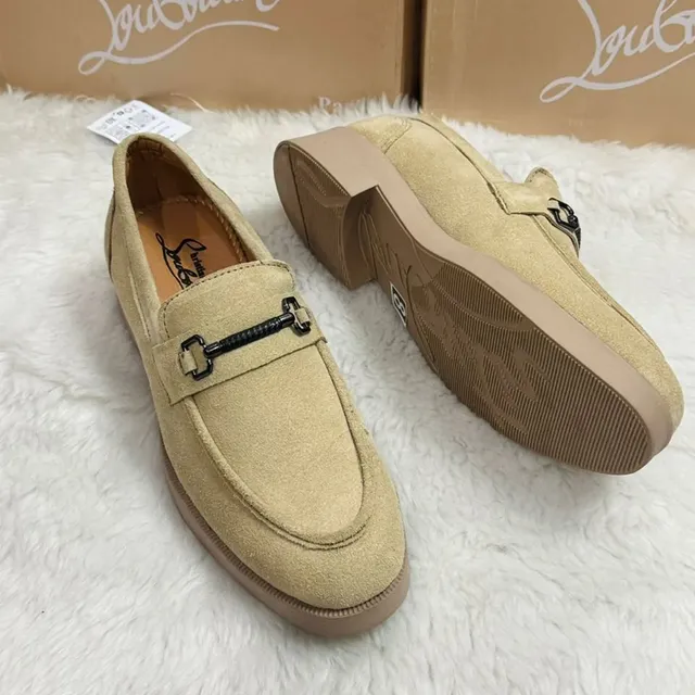 Beige suede men's loafers with black metal detailing displayed on a white fur surface.